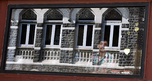 A man looks out of his shop as the Taj Mahal hotel is reflected in the window in Mumbai.