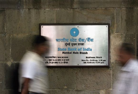 People walk in front of a signboard displayed at the head office of State Bank of India in Mumbai.