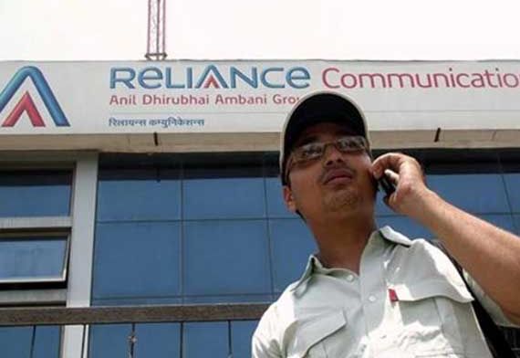 A man talks on a mobile phone in front of an advertisement for Reliance Communications.