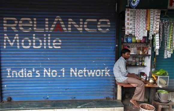A street vendor sells his goods beside a Reliance mobile phone store.