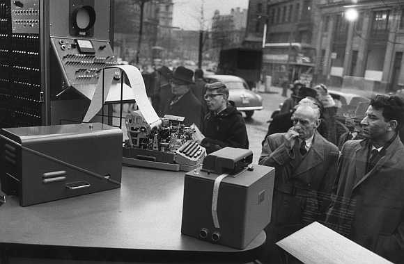 A group of men look at computers in a shop window in 1955.