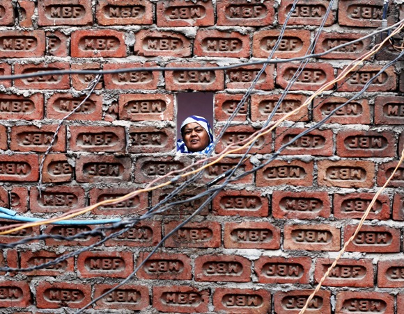 A woman looks from behind a brick wall of her house in the old quarters of Delhi.