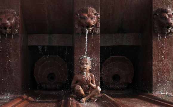 A boy cools himself off as he sits under a fountain on a hot summer day in New Delhi.