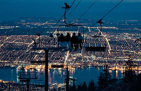 Snowboarders ride a chair lift during night skiing on Grouse Mountain with Vancouver, British Columbia, down below, in Canada.