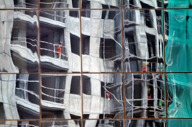 A residential building undergoing construction is reflected on the glass facades of a commercial complex in Chennai.