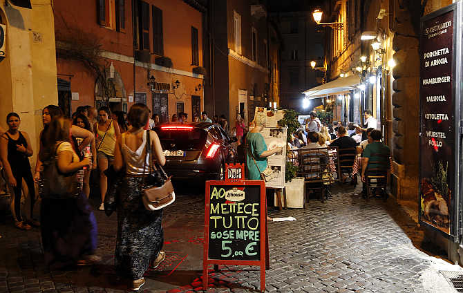 People stroll next to a restaurant along a street in downtown Rome, Italy.