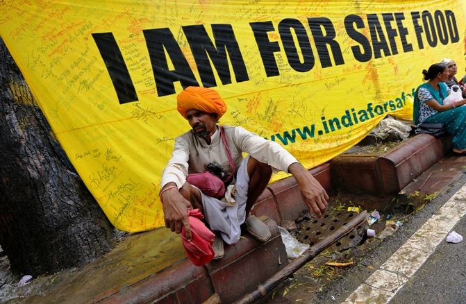 A farmer squats along a footpath near a banner during a day-long protest in New Delhi.