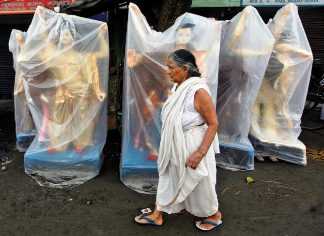 An old woman walks past the plastic wrapped idols of Vishwakarma, the Hindu deity of architecture and machinery, kept on display for sale at a roadside in Kolkata.