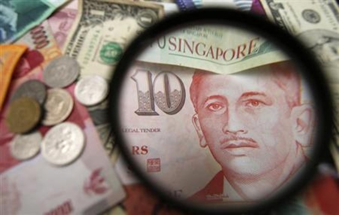 Singapore currency notes are seen through a magnifying glass among other currencies in this photo illustration taken in Singapore 
