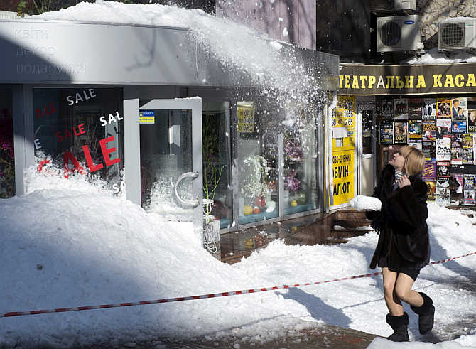 A woman walks on the street as snow falls from a roof after an unusually heavy snowstorm in Kiev, Ukraine.