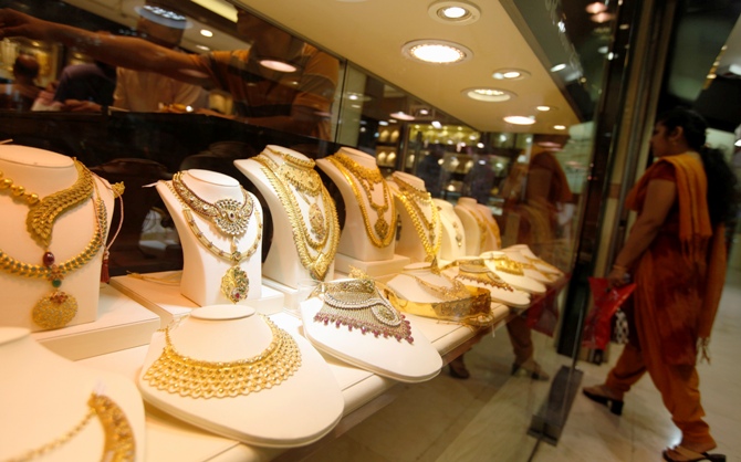 A woman walks past gold jewellery in a display window.
