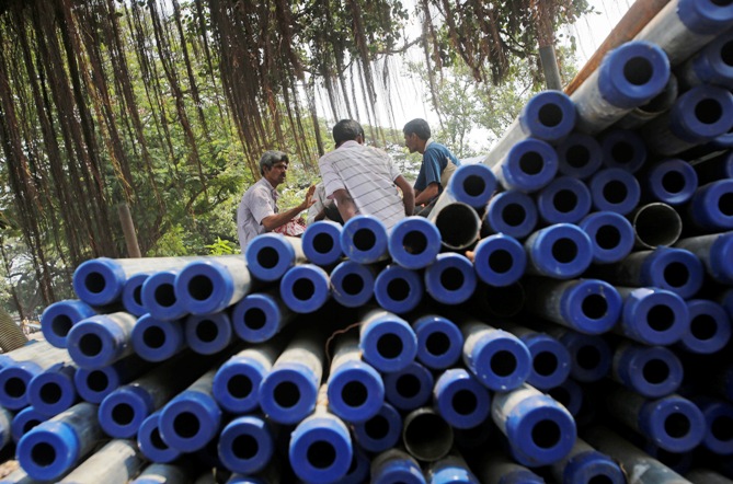 Workers sit on iron pipes before loading them on a truck at an iron and steel market in an industrial area in Mumbai.
