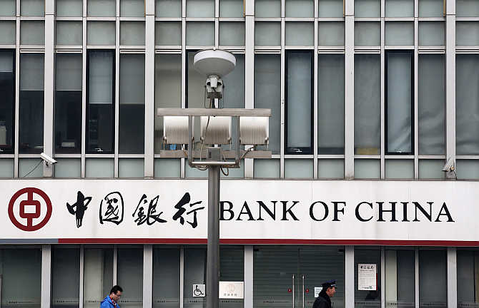 A security official and a man walk past a signboard of Bank of China at its branch in Beijing.