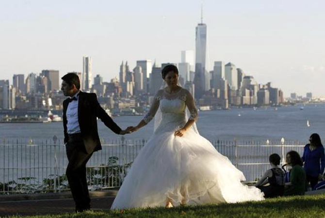 Mustafa Aktas from Ankara, Turkey holds hands with his bride Hatice Yigiter as they walk in front of the skyline of New York's Lower Manhattan and One World Trade Center in a park along the Hudson River in Weehawken, New Jersey.