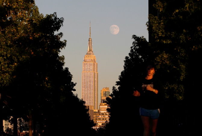 The moon rises at sunset behind New York's Empire State building as a woman runs along a promenade in Hoboken, New Jersey, September 17, 2013.