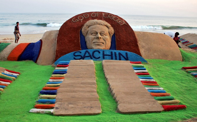 People walk past a sand sculpture of cricketer Sachin Tendulkar created by Indian sand artist Sudarshan Patnaik on a beach in Puri.