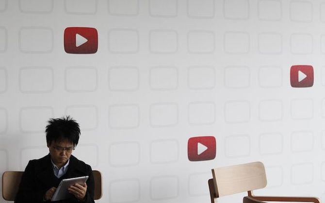 A man uses an Apple iPad tablet in front of a wall featuring the play icons of YouTube at the YouTube Space Tokyo.