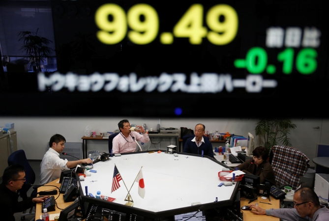 Employees of a foreign currency company work under a screen displaying the Japanese yen's exchange rate against the US dollar, at a dealing room in Tokyo November 13, 2013.