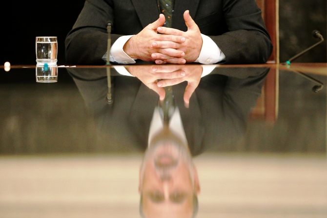 US Federal Reserve Chairman Ben Bernanke is reflected in a glass table top as he holds town hall event for teachers at the Federal Reserve Board's building in Washington November 13, 2013.