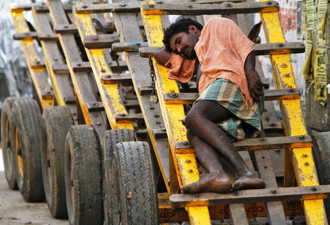A labourer takes a nap on a wooden cart at a wholesale vegetable market in Chennai.