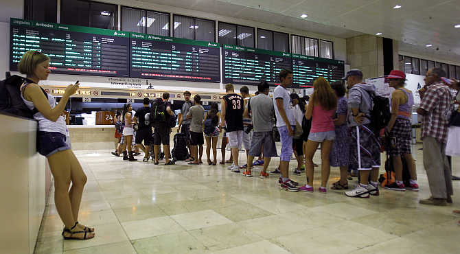 A passenger uses her mobile phone as others queue in front of an information counter at a railway station in Barcelona, Spain.