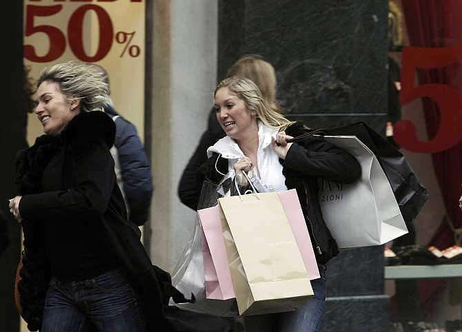 Women run past a clothing boutique in Milan, Italy.