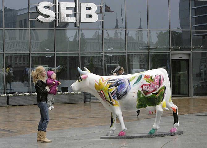 A woman lifts a child to look at a painted model of a cow in front of SEB bank branch in Europa business centre in Vilnius, Lithuania.