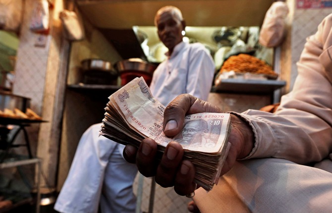 A street side restaurant owner holds a bundle of Indian currency notes as he sits outside his restaurant in New Delhi.