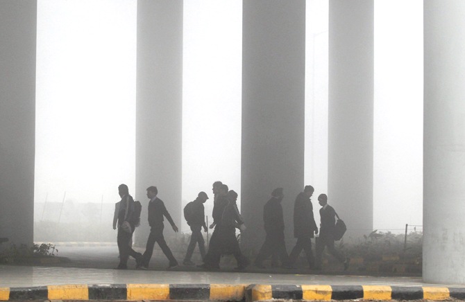 Airport staff walk towards the main terminal amid heavy fog in New Delhi.