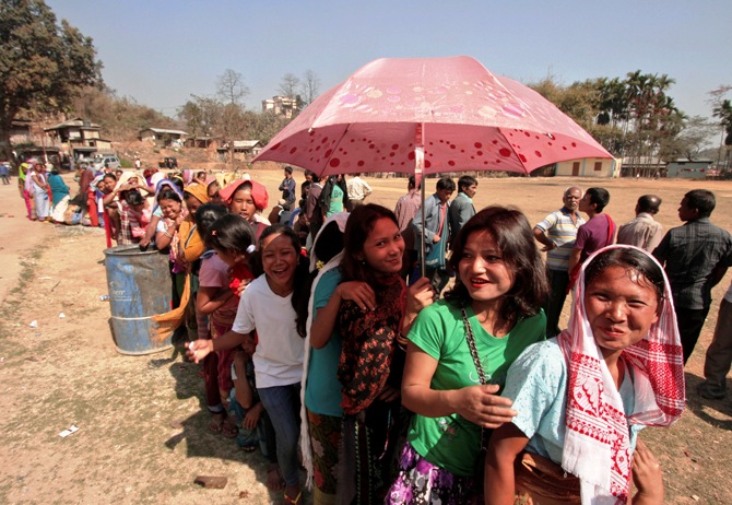 A woman shields herself from the sun with an umbrella as she and others queue to cast their vote at a polling station at Byrnihat, in the Ri-Bhoi district in the eastern Indian state of Meghalaya.