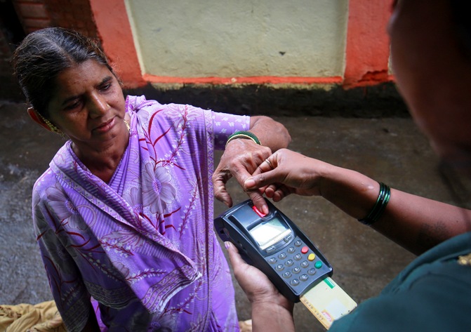 A customer gives her finger impression to update her smart card after she gave her money to a coordinator who works for Financial Information Network and Operations Ltd in Wavanje village of Raigad district.