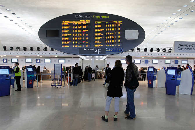 Passengers look at a flight departure information board in a terminal at the Charles-de-Gaulle airport in Roissy, near Paris.