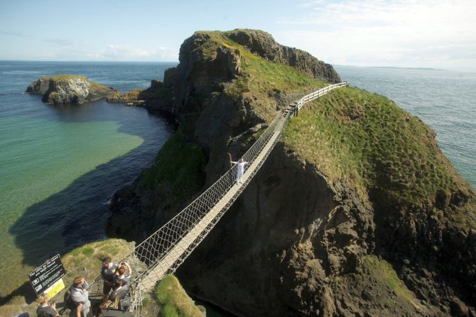 Torchbearer Denis Broderick holds the Olympic Flame on the Carrick-a-Rede rope bridge.