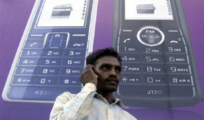 A man speaks on a mobile phone in front of a billboard.