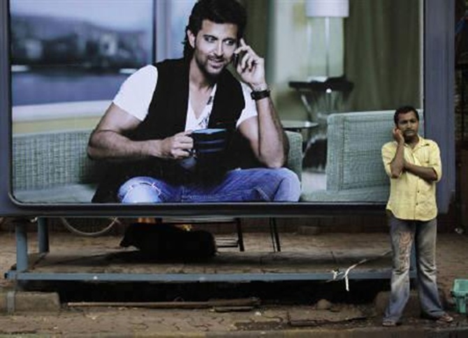 A man makes a phone call on his mobile phone in front of an advertisement  in Mumbai.