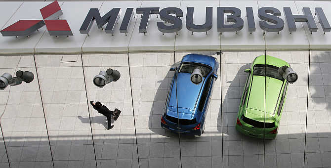 Mitsubishi Motors's vehicles and a passer-by are reflected on an external wall at the company headquarters in Tokyo.