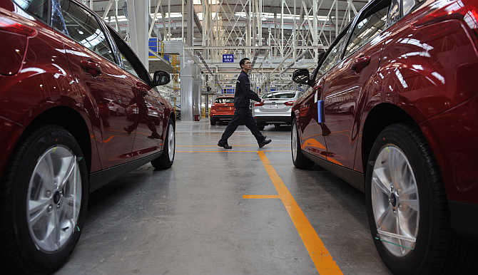 An employee walks past newly assembled cars at a Ford manufacturing plant in Chongqing municipality in China.