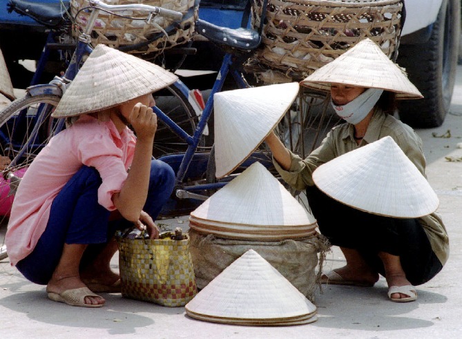 A Vietnamese woman buys conical hats called 'non' from a sidewalk vendor in Hanoi.