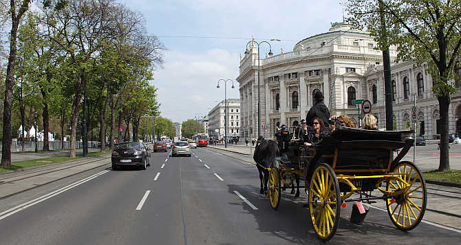 A traditional Fiaker horse carriage passes Burgtheater theatre on Dr-Karl-Lueger-Ring street in Vienna, Austria.