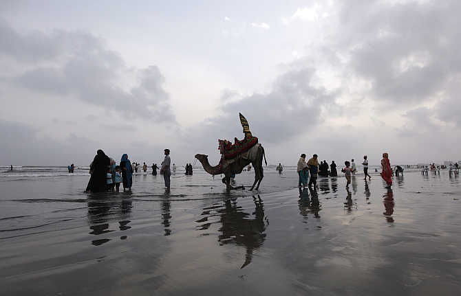A man talks to customers while offering them a camel ride along Karachi's Clifton Beach, Pakistan.