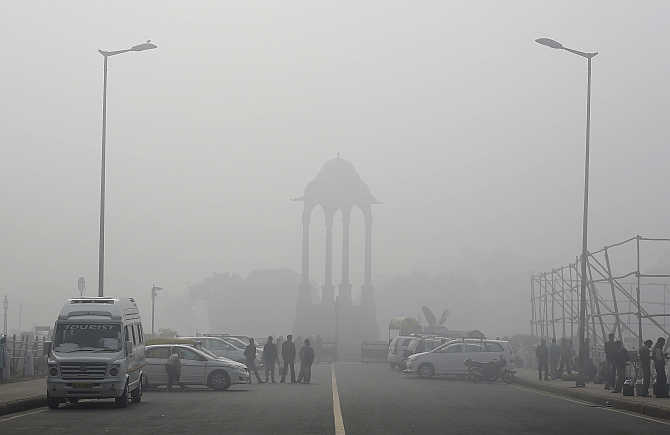 Vendors selling drinks stand beside vehicles near the India Gate war memorial on a smoggy day in New Delhi.