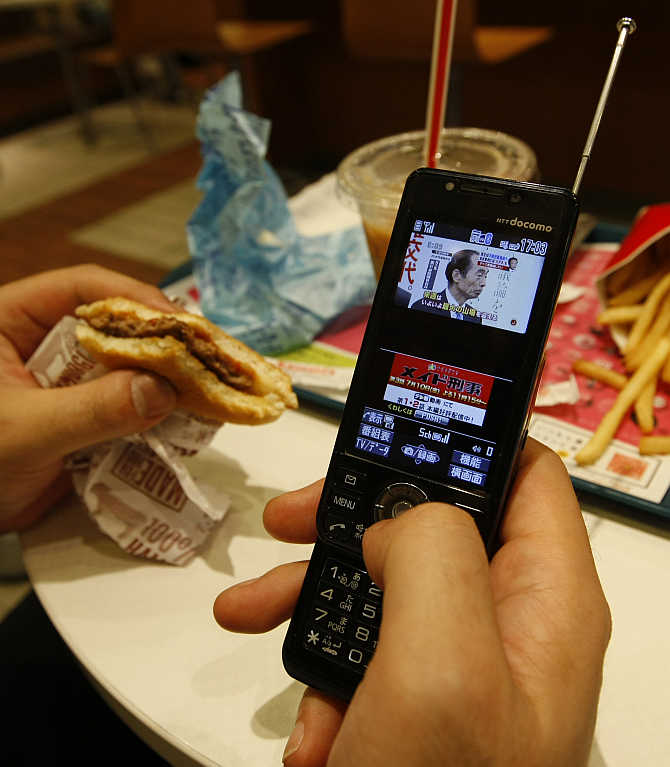 A man watches television through his mobile phone at a fast food restaurant in Tokyo, Japan.