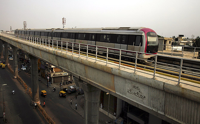 A Namma Metro (Kannada for Our Metro) train travels along an elevated track as traffic passes below in the Indira Nagar area of Bangalore.