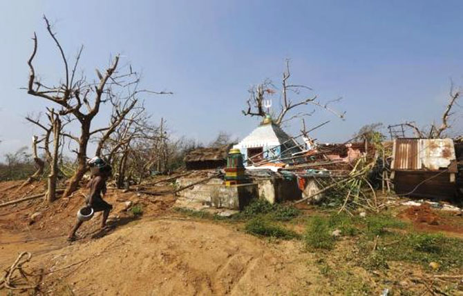 A man carries his belongings as he walks past a damaged temple after Cyclone Phailin hit Arjyapalli village, in Ganjam district in Odisha.