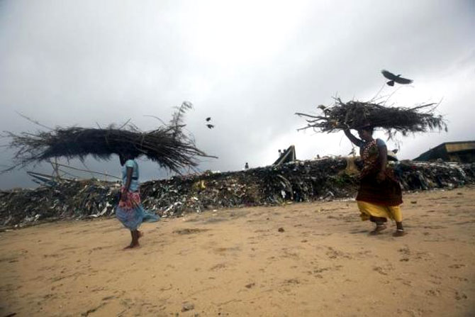 Fisherwomen carrying wood walk past an eroded shore after Cyclone Phailin hit Puri.