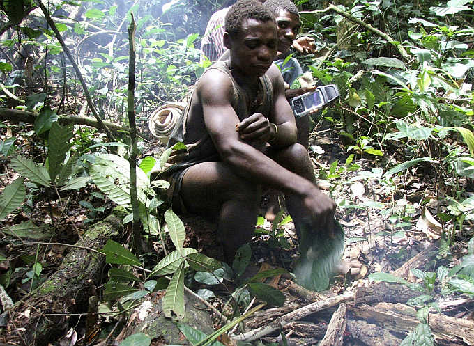 Baka, a Mbendjele pygmy, stops to make a fire in the northern forests of the Congo Republic while another behind him holds a Global Positioning System handset.