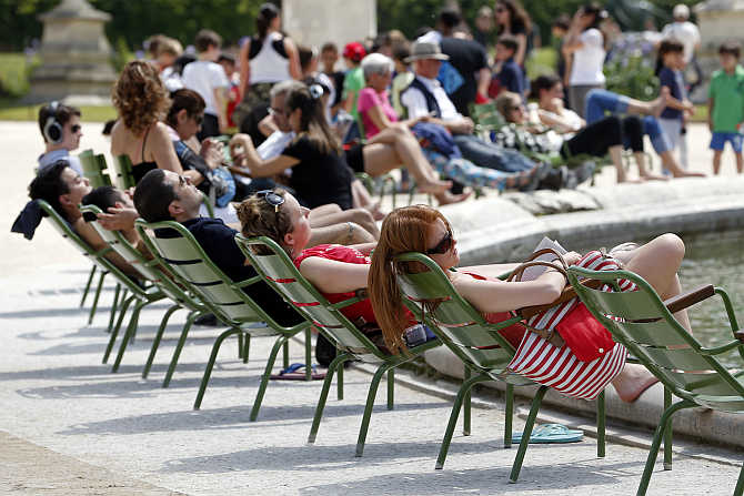 People relax in chairs around a fountain as they take in the sun in the Tuileries Garden in central Paris, France.