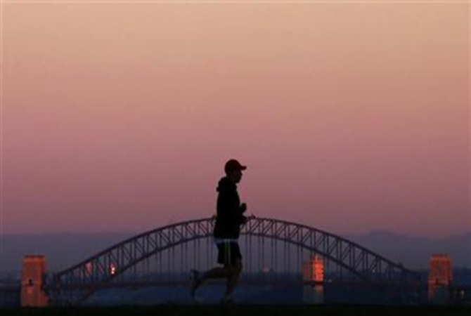 A man runs across a hill in front of the SydneyHarbourBridge under a smoke tinted sky at daybreak.