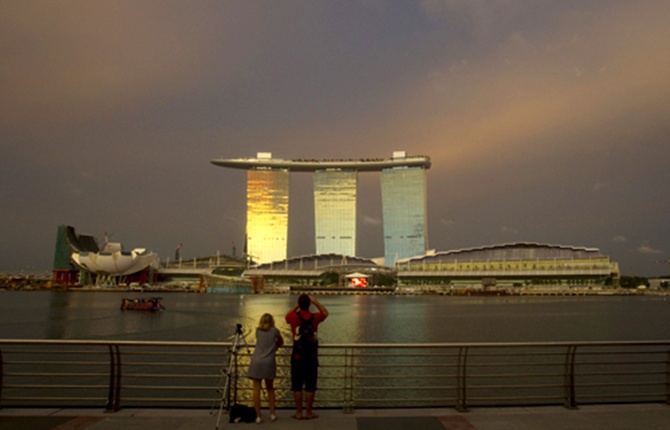 Tourists stand at a promenade across the water from the Marina Bay Sands integrated resort in Singapore.
