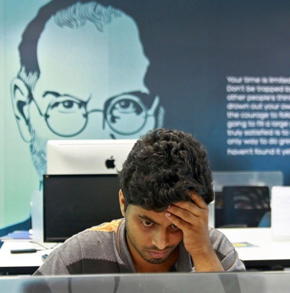 An employee works on a computer terminal against the backdrop of a picture of late Apple co-founder Steve Jobs.